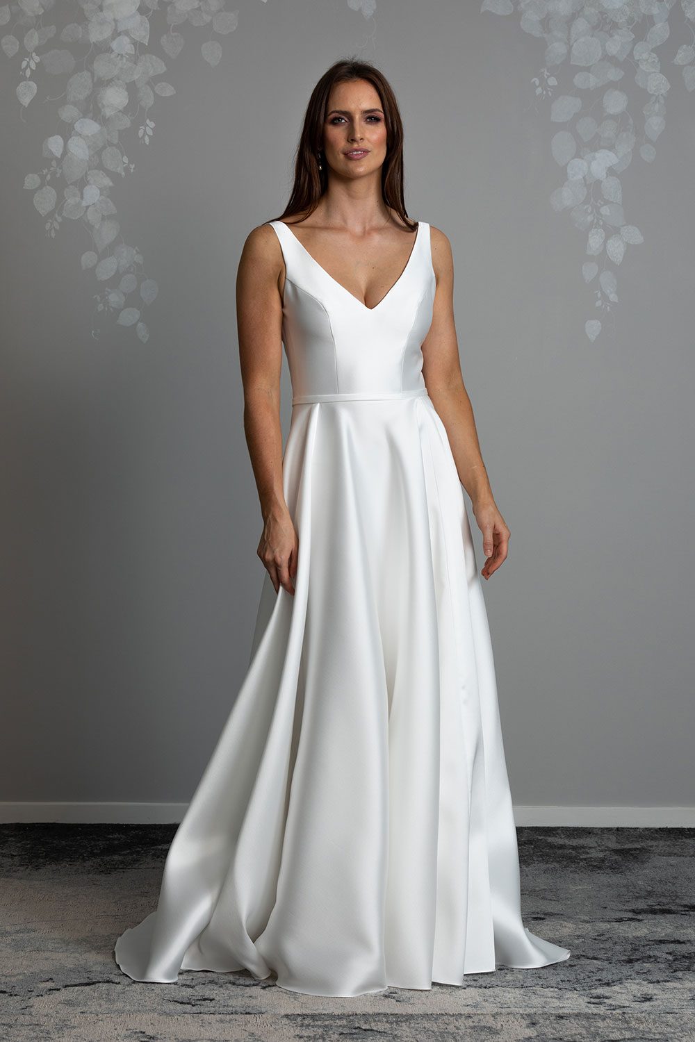 Madison Wedding gown from Vinka Design - This gown is both classic and contemporary, made beautifully with luxurious Mikado satin. The bodice is structured with a deep V-neckline and a squared, low back. Full length view of model with classic and modern dress made of Mikado satin with deep V bodice and irregular folded skirt