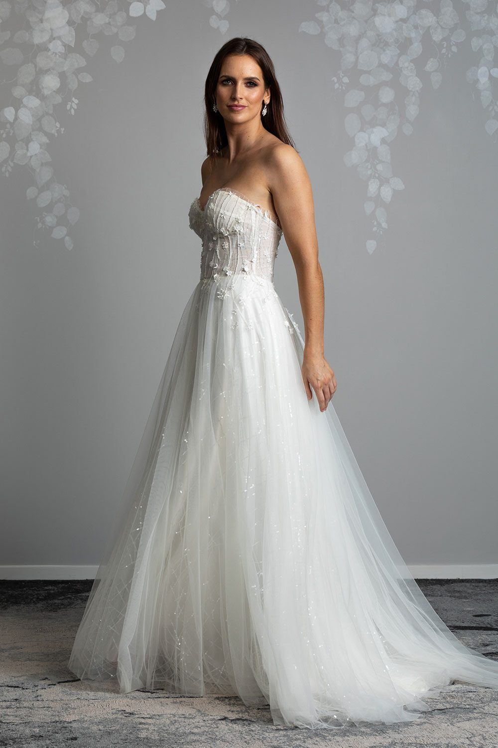 Hikari Wedding gown from Vinka Design - This modern wedding dress has a structured semi-sheer bodice with hand-appliqued lace of stars and flowers. The skirt is made with multiple layers of soft tulle. Profile view of model wearing stunning contemporary gown with feminine appeal
