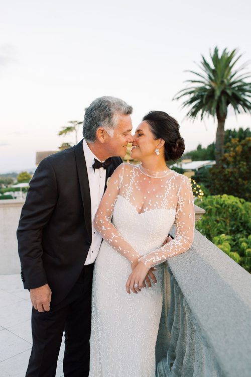Bride wearing bespoke gown by Auckland wedding dress designer Vinka Design, with a high neckline and delicate spotted embroidery - profile with groom