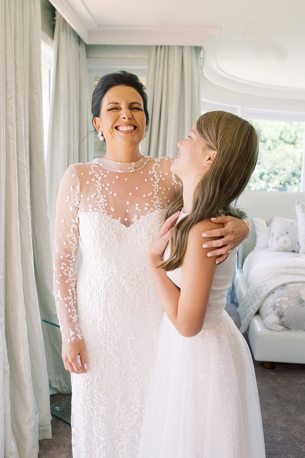 Bride wearing bespoke gown by Auckland wedding dress designer Vinka Design, with a high neckline and delicate spotted embroidery - bride and bridesmaid laughing