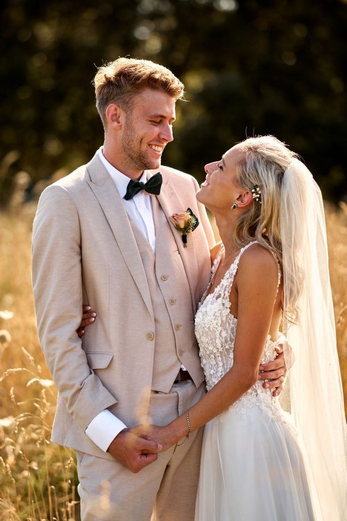 Bride wearing bespoke gown made of silk chiffon with delicate flower lace bodice by Vinka bridal designer Auckland - with groom looking at each other in field