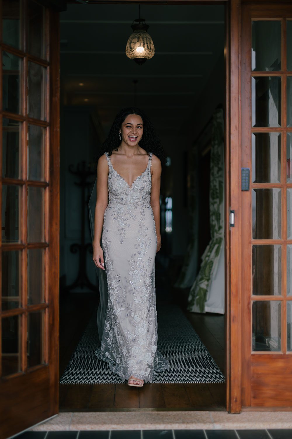 Bride wearing Kazumi Gown in soft grey with hand embellished lace and a low back - in doorway