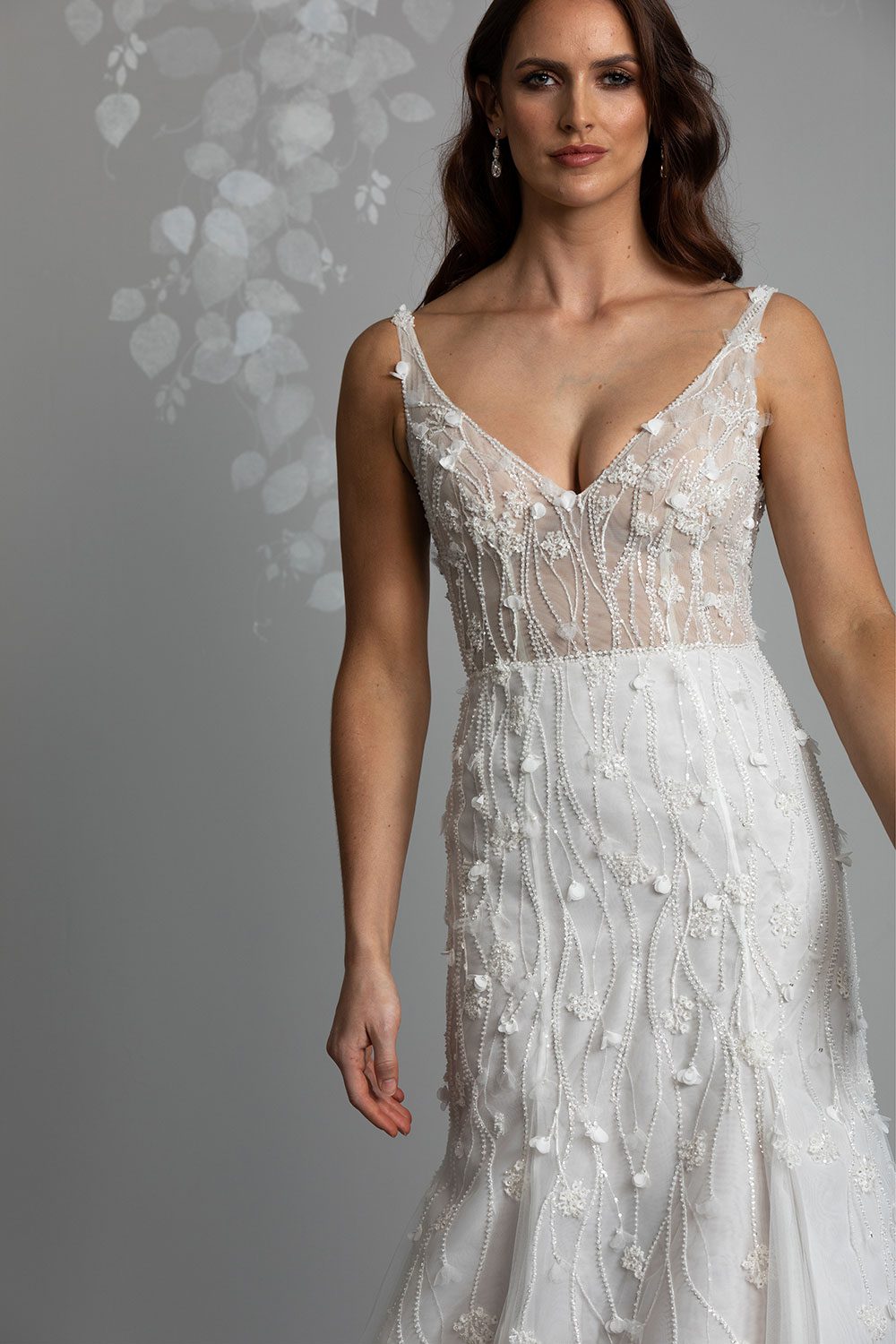 Bronte Wedding Dress by Vinka Design - Featuring a form sculpting mermaid silhouette that embraces the wearer's curves, and intricately embroidered, beaded, botanical lace that trails seamlessly from the bodice into the skirt. Crafted on a semi-sheer base, the bodice boasts a V-neckline and beautiful low V-back. Artfully constructed with layers of dreamy, yet dramatic silk organza and soft tulle, added flare and fullness is achieved through the skirt which fans into a sweeping opulent train. Full length view of model wearing V-neckline bodice with intricately embroidered beaded botanical lace with a dreamy silk organza and soft tulle skirt
