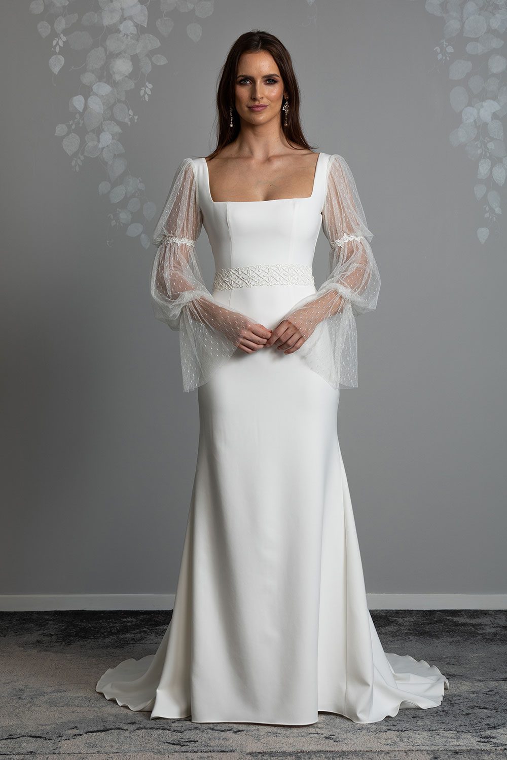Eden Wedding Dress by Vinka Design - Featuring a square neckline that draws the eye to the wearer's décolletage and dreamy, soft, tulle puff sleeves with corded embroidered lace adorning the arms in tiers. The low back is complemented by a curved, scoop cut, with delicate self-covered crepe button embellishments trailing down the spine. Full length view of model wearing square neck bodice with soft tulle puff sleeves and embroidered lace