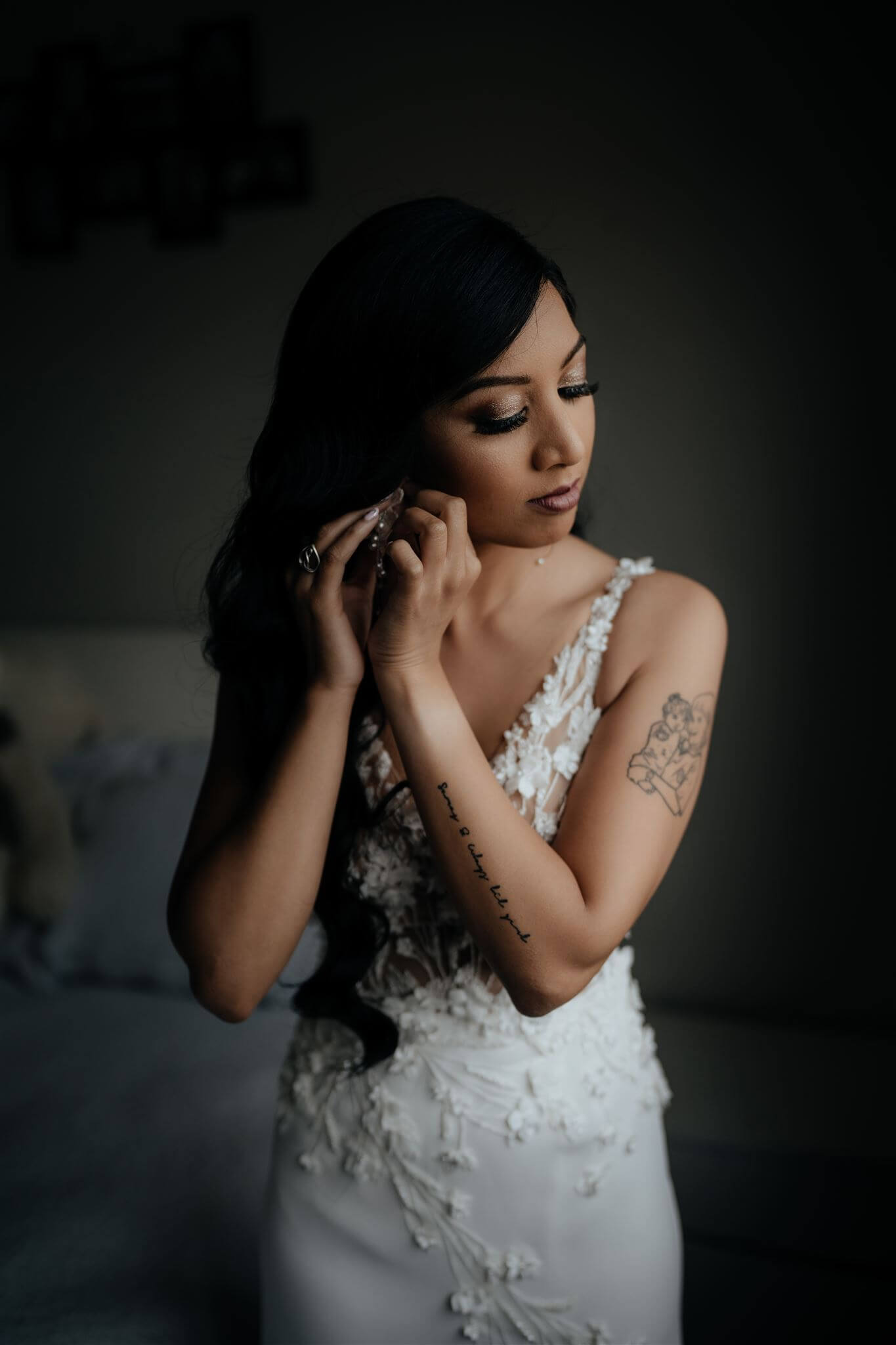 Vinka Design Real Wedding with Vinka Bride Prianka in full length wedding dress - bride poses showing detail of dress with stunning lace underlayer with beautiful detail - putting on earrings