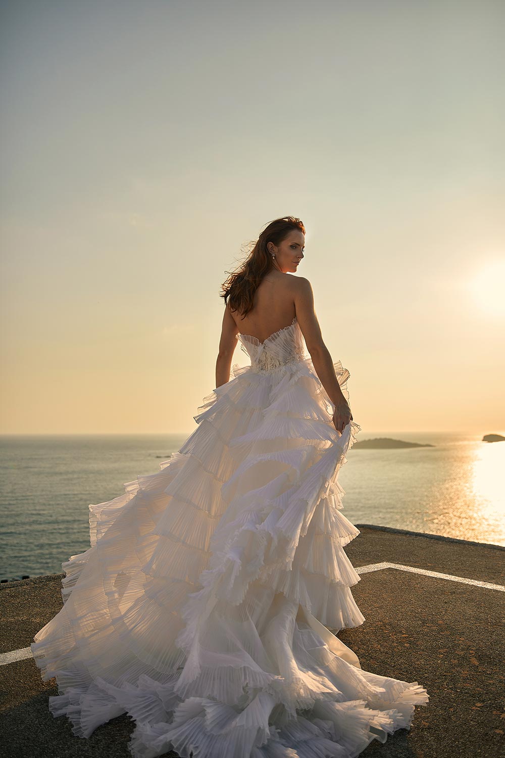 Experience Antonia, a bridal gown with drama & detail. Features 3D lace, a semi-sheer bodice, and layers of pleated silk draping on a ball gown silhouette. By Vinka Design